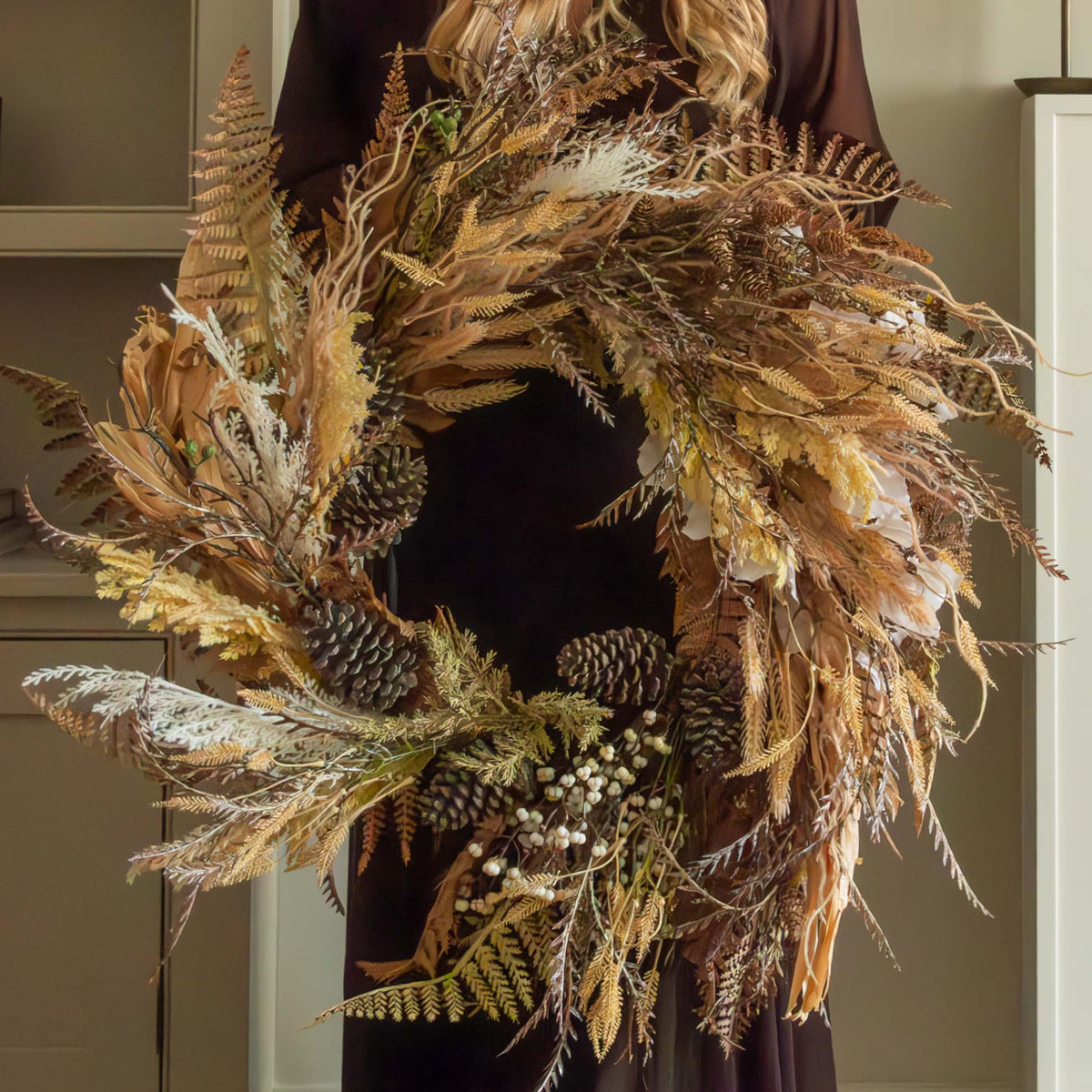 Woman holding a large dried wreath in a cozy living room with a fireplace.