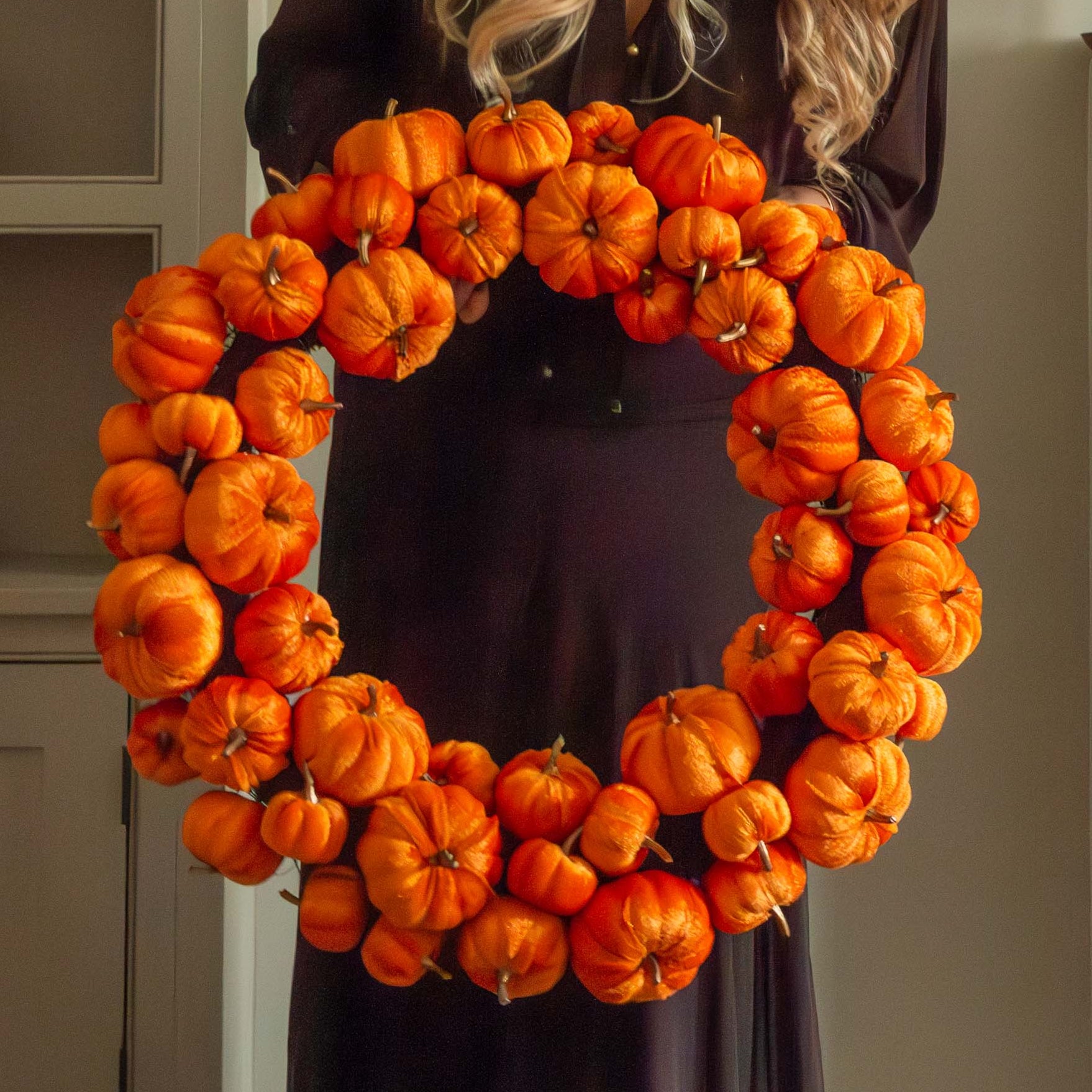 Woman holding a large orange pumpkin wreath in a cosy living room. close up detail