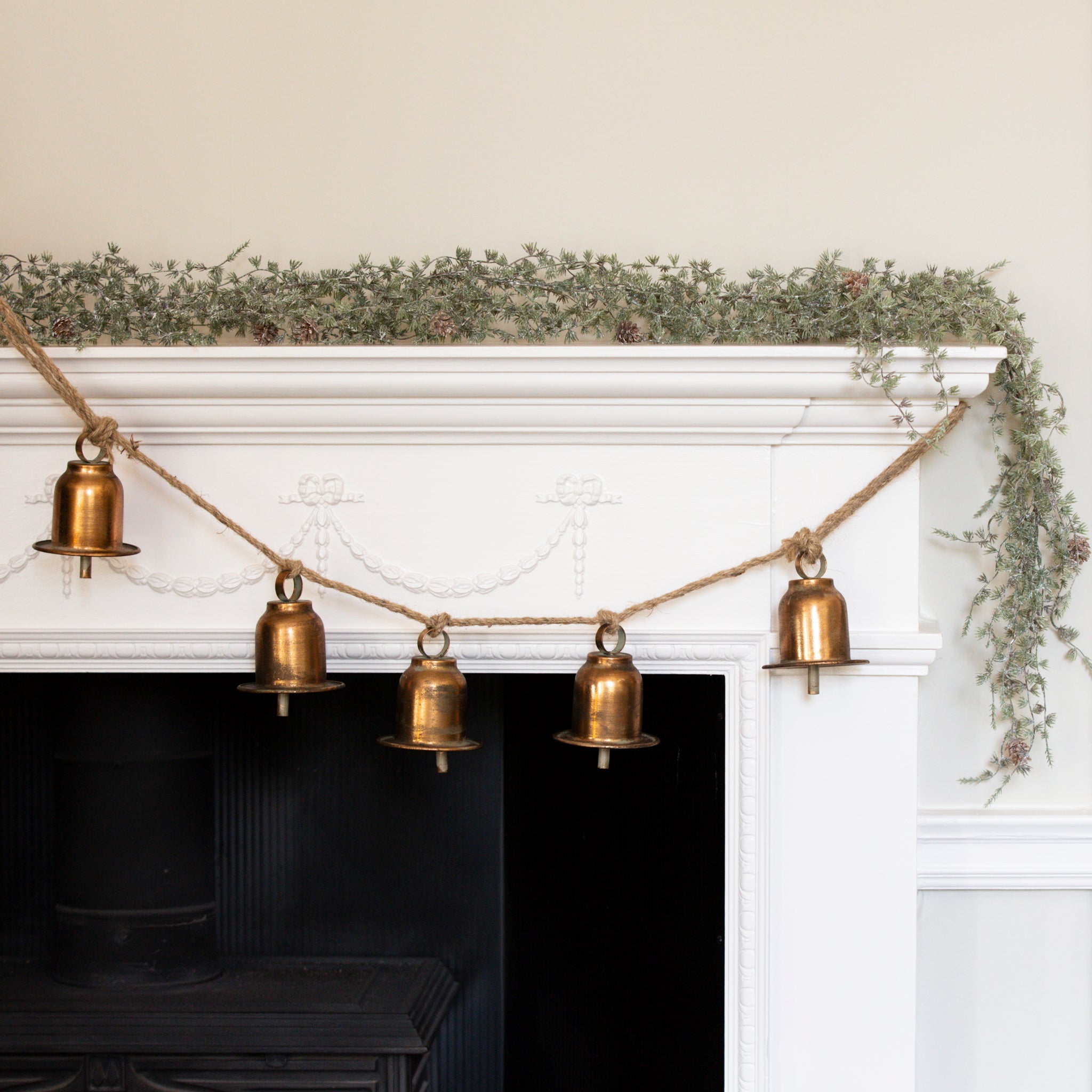 Charles Ted Bell Garland with rustic metal bells hanging on a jute rope across a white mantel decorated with greenery