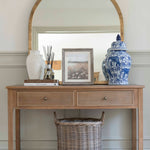 A decorative Chinoiserie pot with lid on a wooden table, alongside a round mirror and other home décor items.