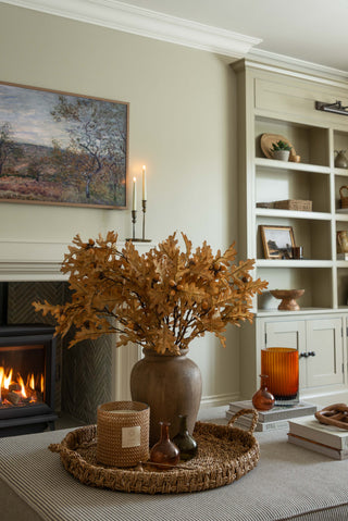 Faux oak leaves with acorns styled in a rustic vase on a coffee table