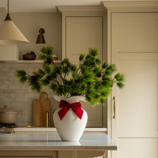 Faux pine cone sprays in a white vase with a red ribbon in a country kitchen