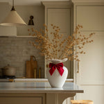 White vase with dried flowers and a red bow on a kitchen counter