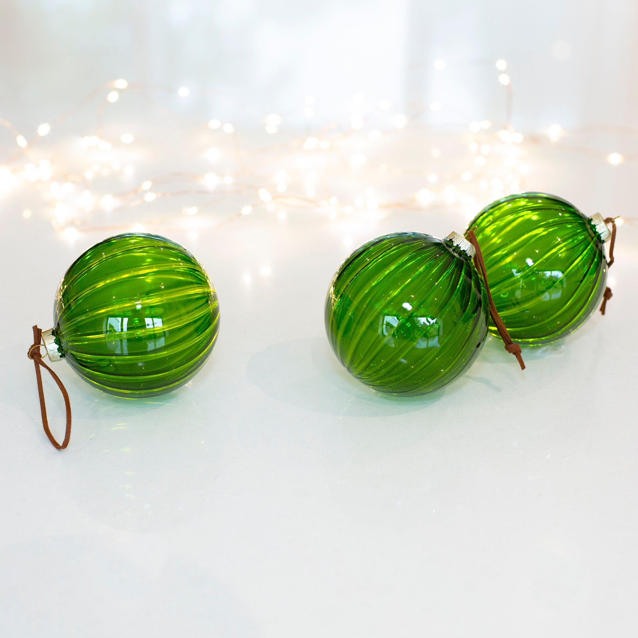 Charles Ted Green Glass Ribbed Baubles displayed on a white surface with fairy lights 