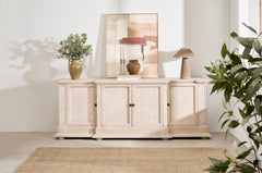 A white oak sideboard with four doors and bronze hardware, placed in a room with decorative items on top and a plant to the side.