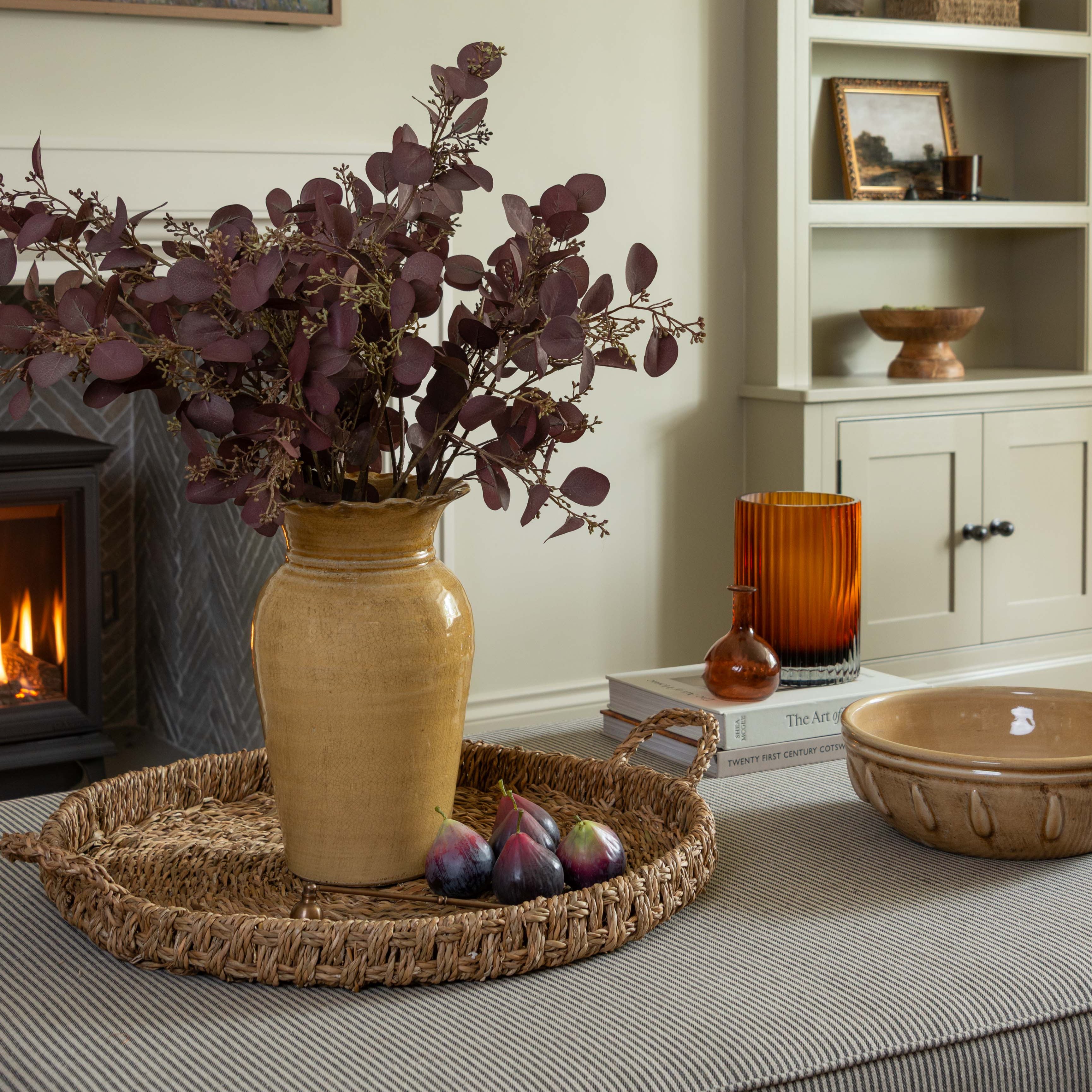 Decorative setting with a vase of purple flowers on a tray, books, and a candle in a cozy room.