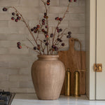 Beige vase with branches on a kitchen counter with a tiled backsplash.