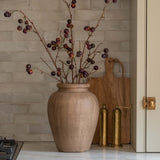 Beige vase with branches on a kitchen counter with a tiled backsplash.