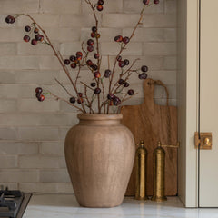 Beige vase with branches on a kitchen counter with a tiled backsplash.