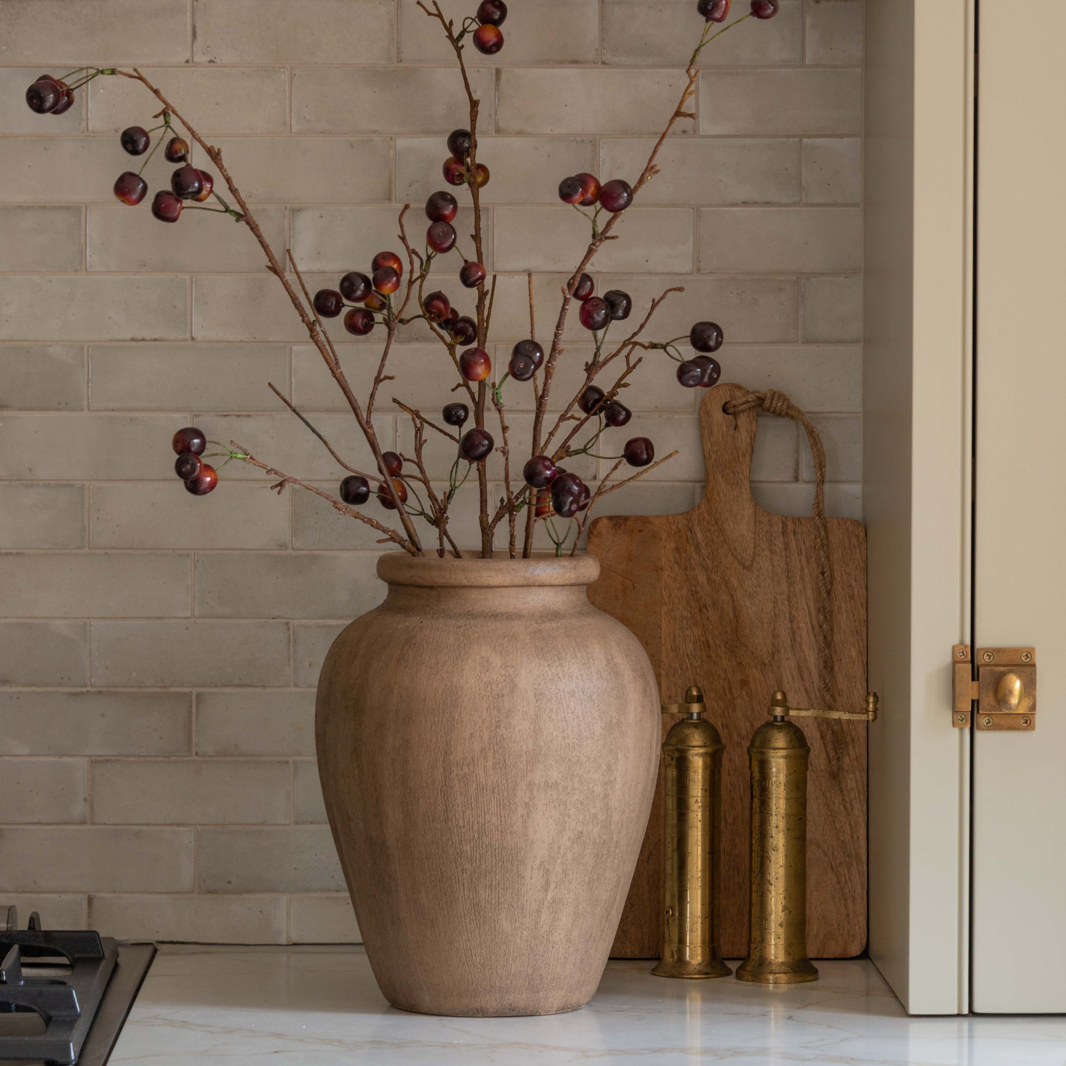 Beige vase with branches on a kitchen counter with a tiled backsplash.