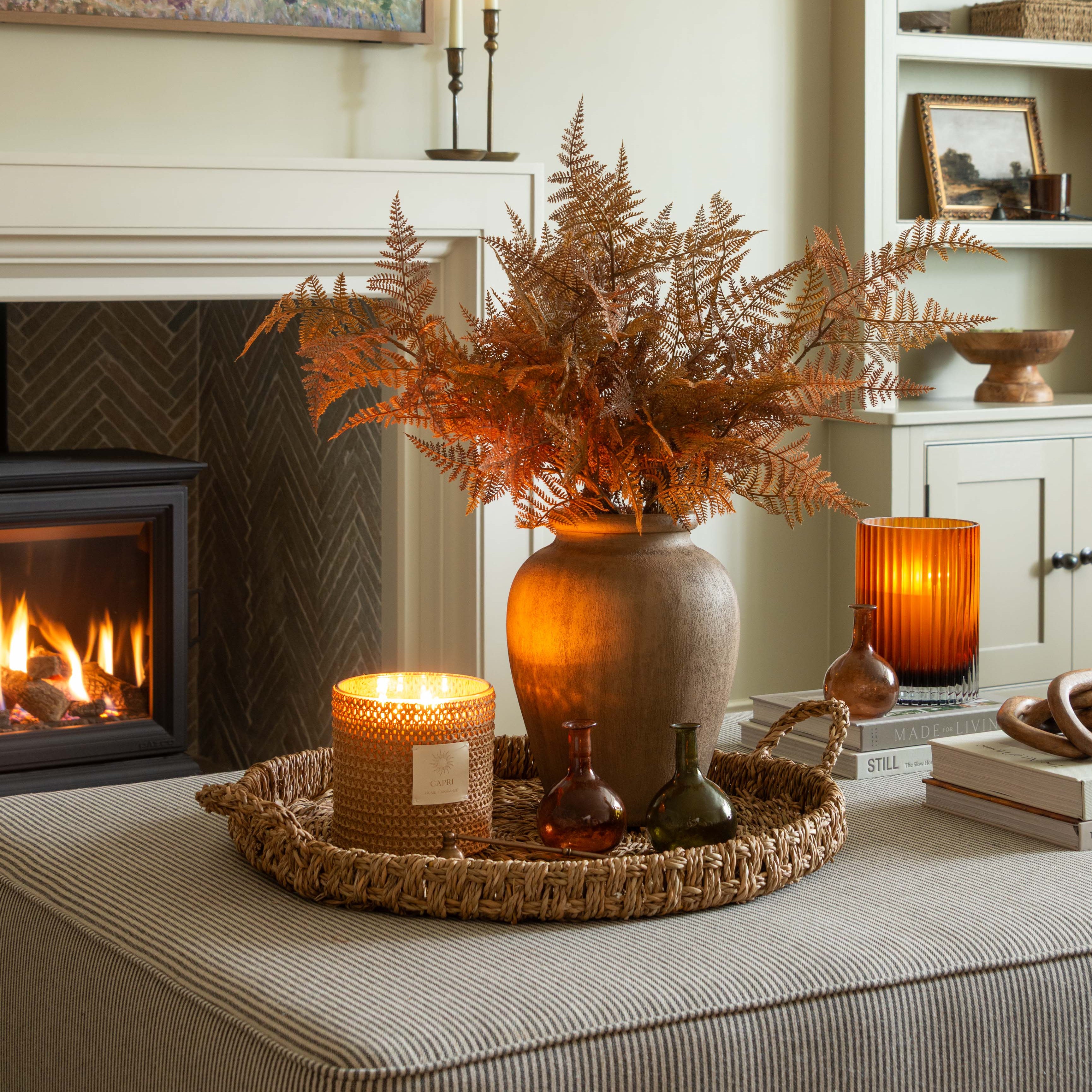 Decorative setting with a vase of dried ferns, candles, and a painting in a living room.