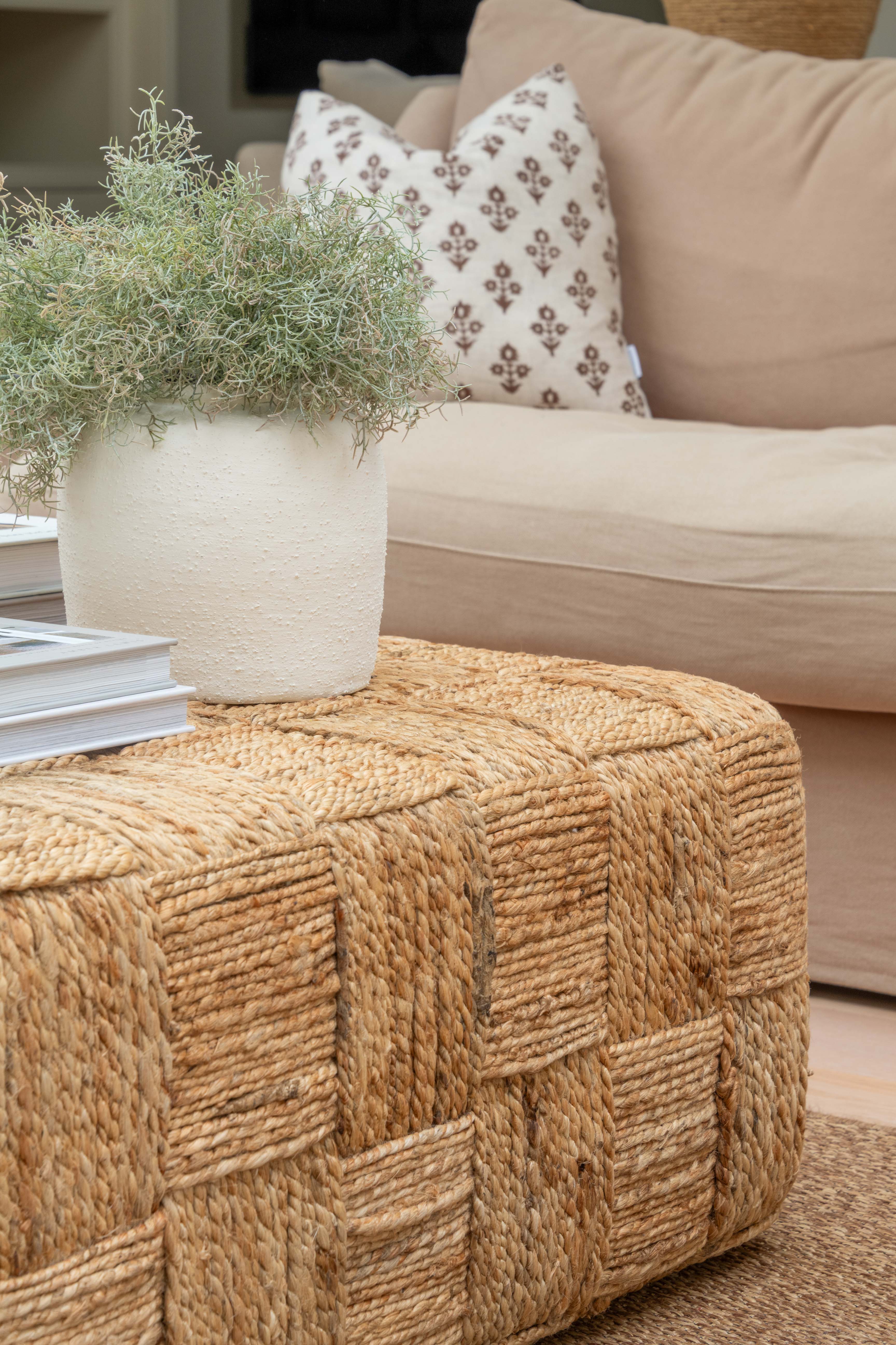 Woven ottoman with a plant and pillows on a beige sofa