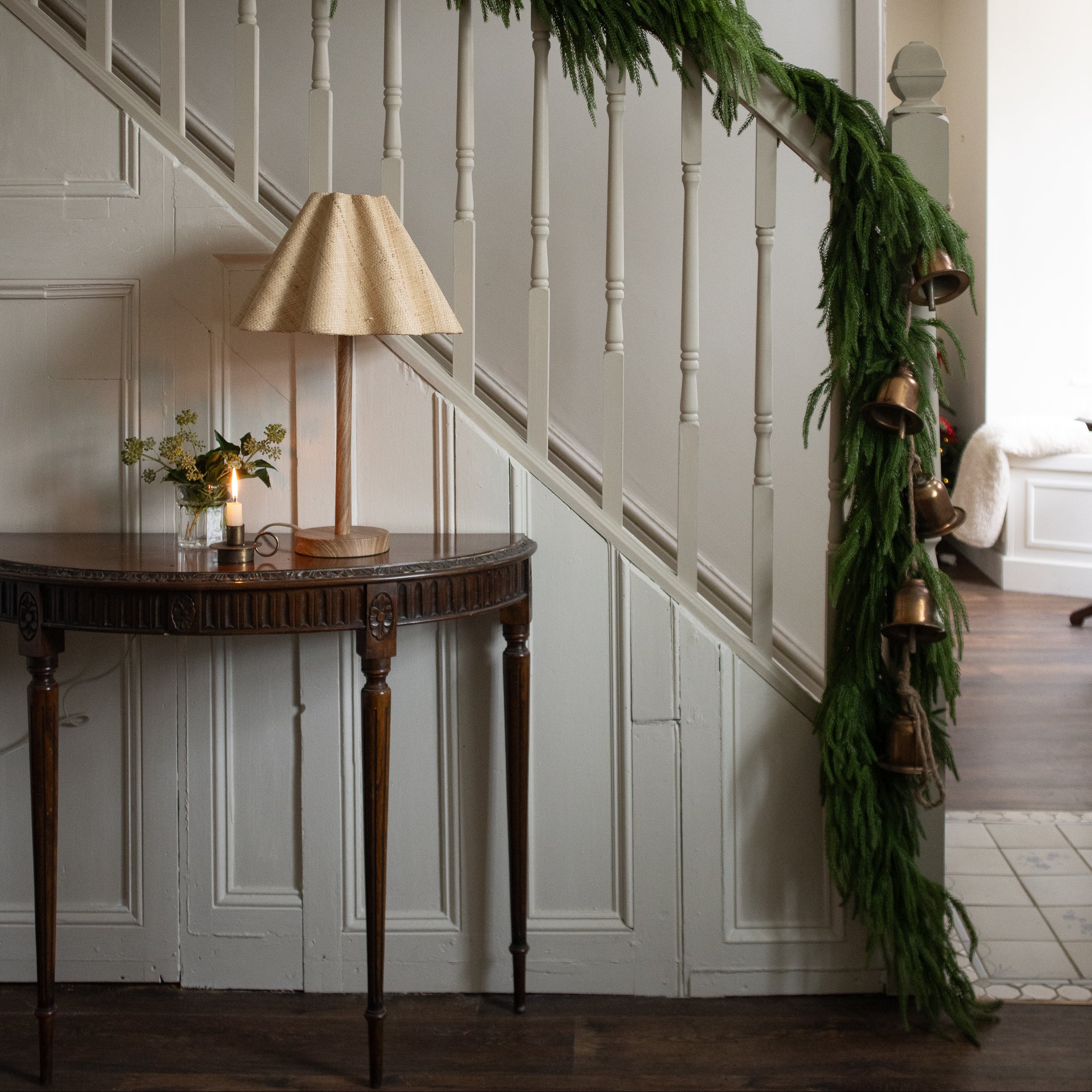 Decorative green garland on a staircase wall with a table and lamp in the foreground.