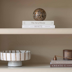 Charles Ted Striped Footed Terracotta Bowl with vertical neutral stripes displayed on a shelf