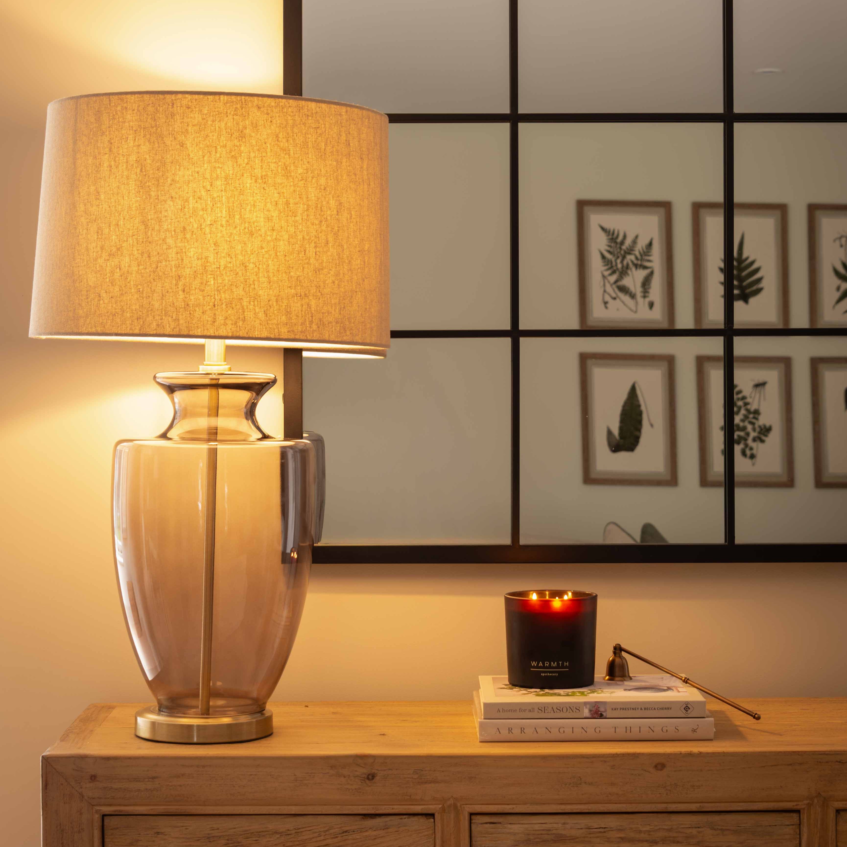 Decorative lamp on a wooden side table with a mirror and framed pictures in the background.