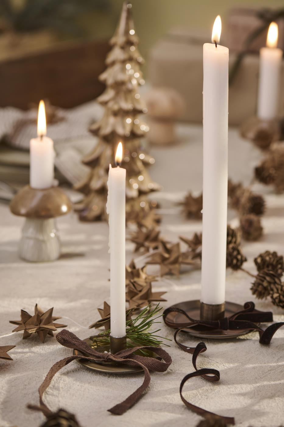 White candles tied with brown velvet ribbon on holiday table setting