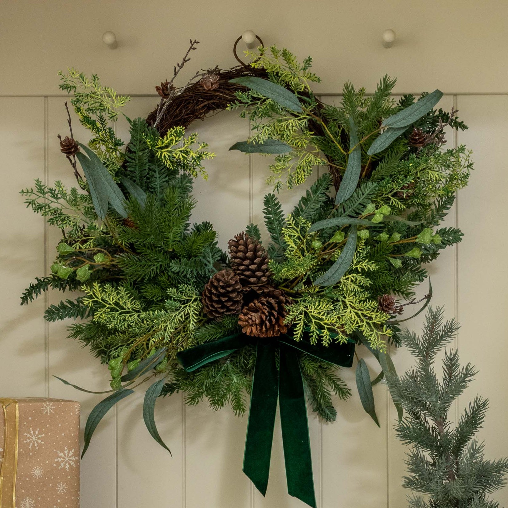 Decorative setup with a wreath, gift boxes, and small trees inside a white cabinet.