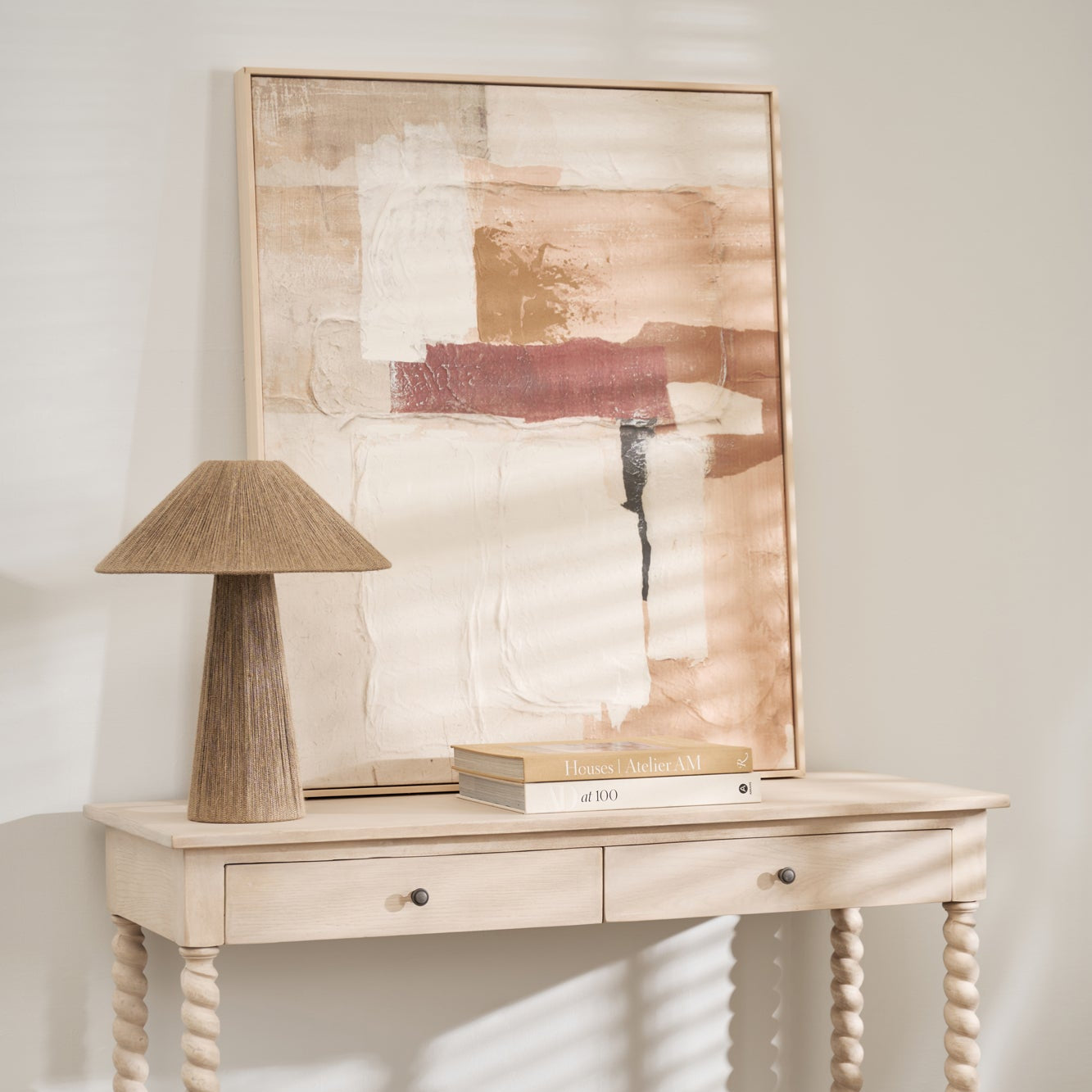 Vertical abstract art piece on console table beside a textured lamp and interior books.