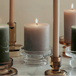 Collection of lit candles in various holders on a neutral background