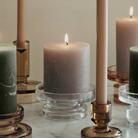 Collection of lit candles in various holders on a neutral background