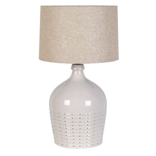 A table lamp with a glossy white ceramic base featuring horizontal slotted detailing and a textured beige linen drum shade, shown against a plain white background.