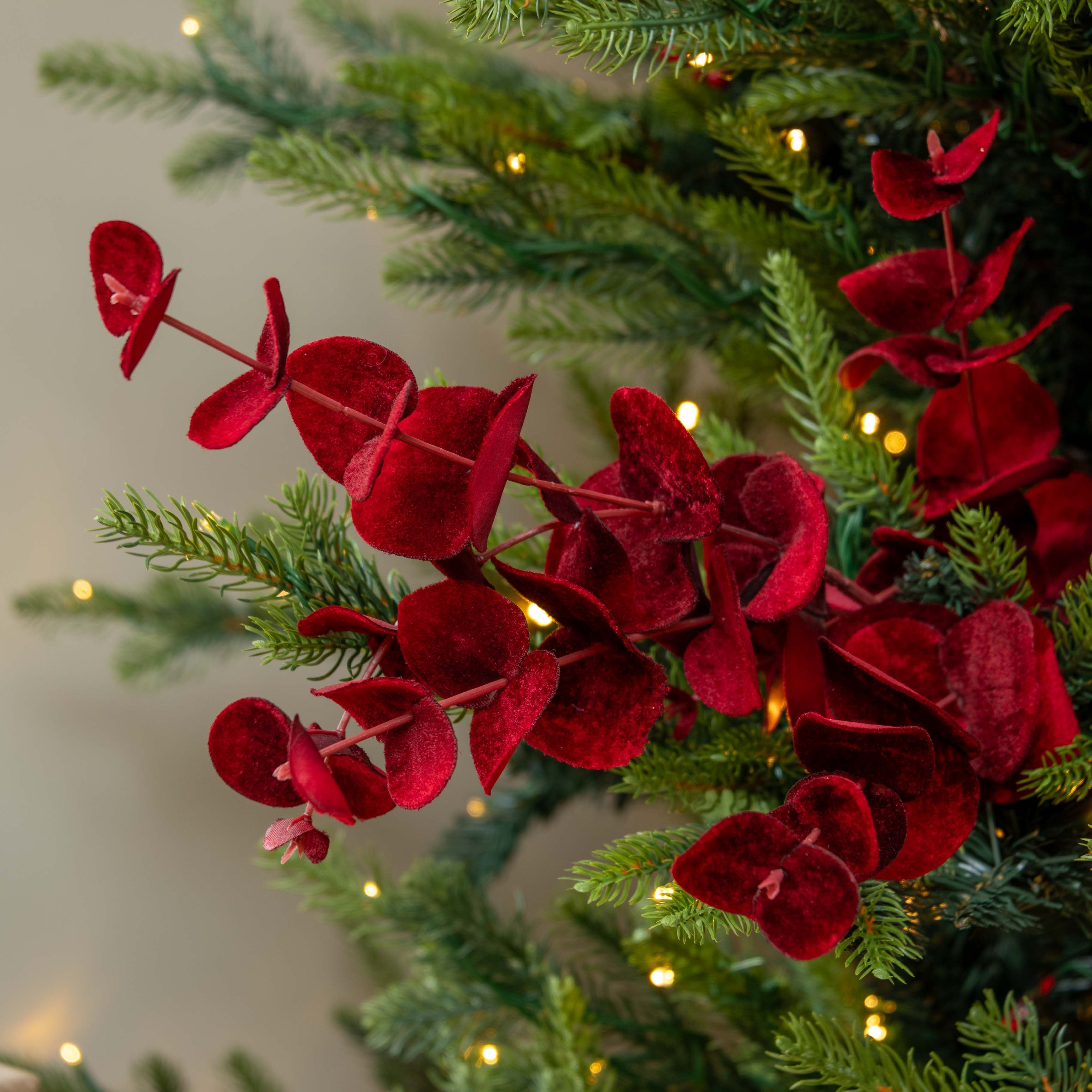 Decorative red flowers on a Christmas tree with lights in the background