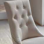 Close-up of a beige upholstered chair with button tufting.