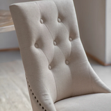 Close-up of a beige upholstered chair with button tufting.