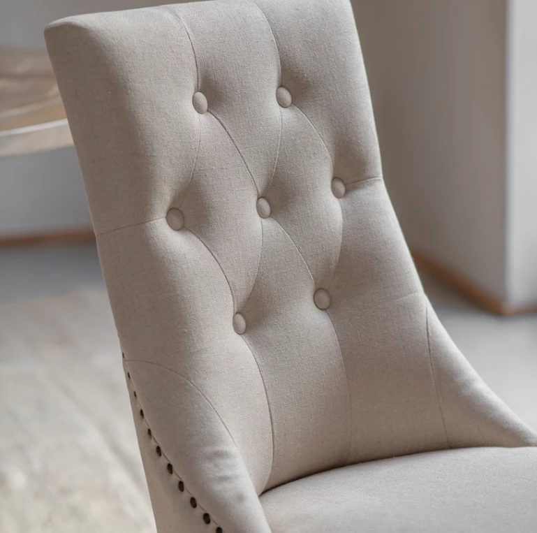 Close-up of a beige upholstered chair with button tufting.