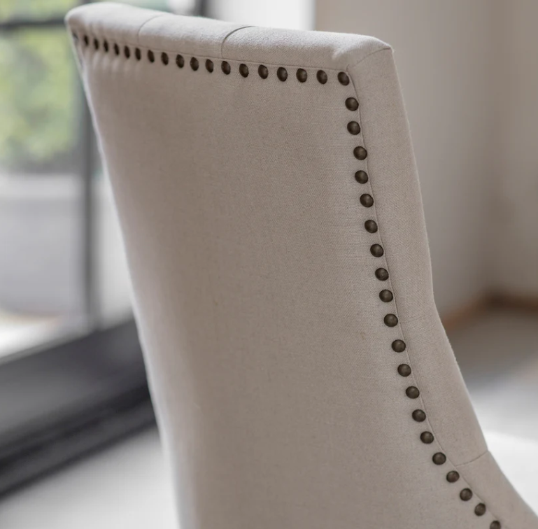 Beige upholstered chair with nailhead trim in a blurred indoor setting