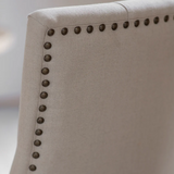 Close-up of a beige upholstered chair with nailhead trim on a blurred background