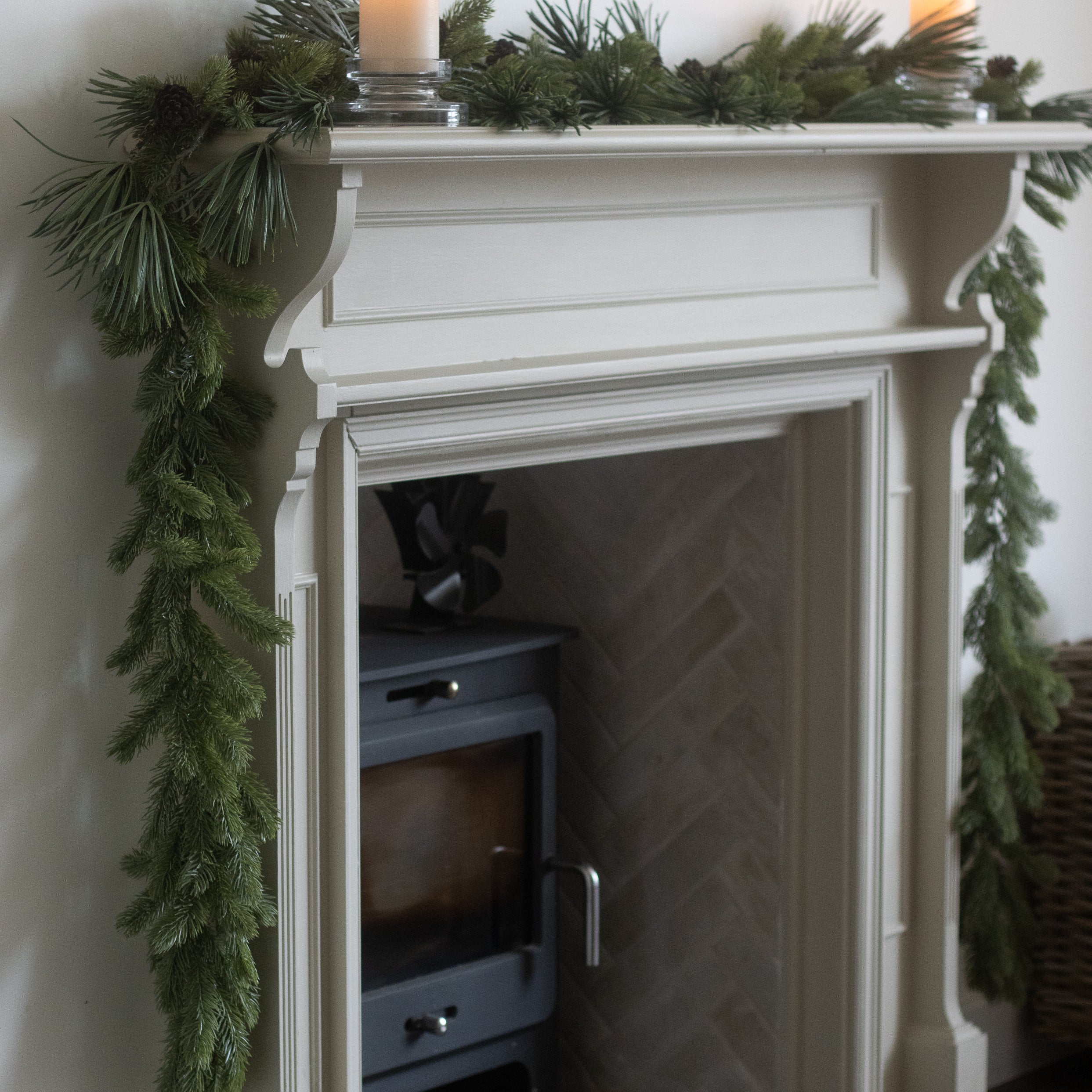 White fireplace with green garland and candles on a white wall