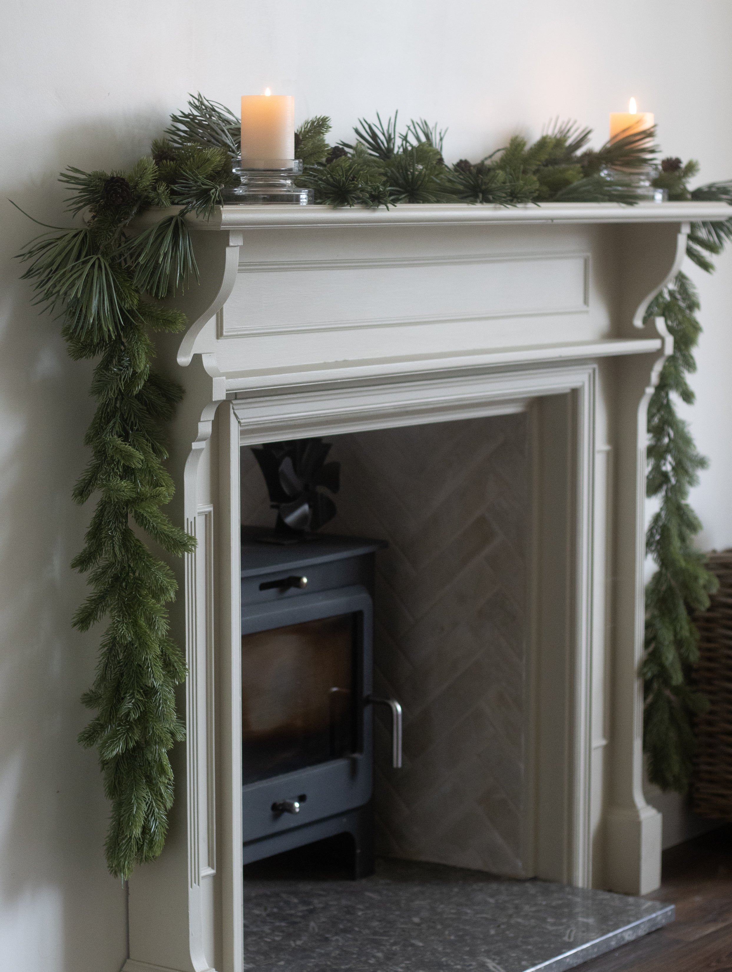 White fireplace with green garland and candles on a white wall