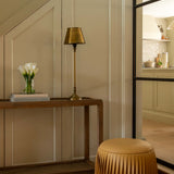 Modern interior with a wooden console table, gold lamp, and beige stool.