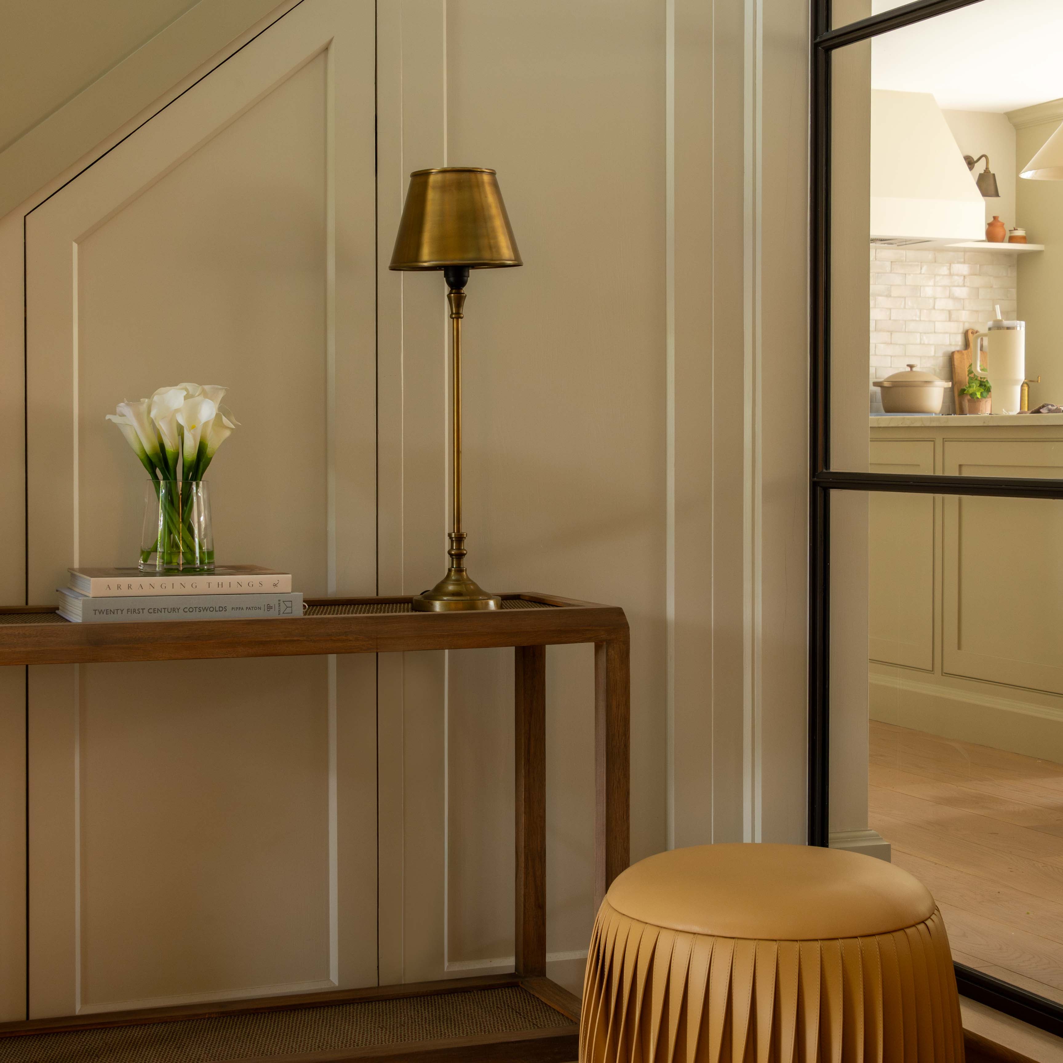 Modern interior with a wooden console table, gold lamp, and beige stool.