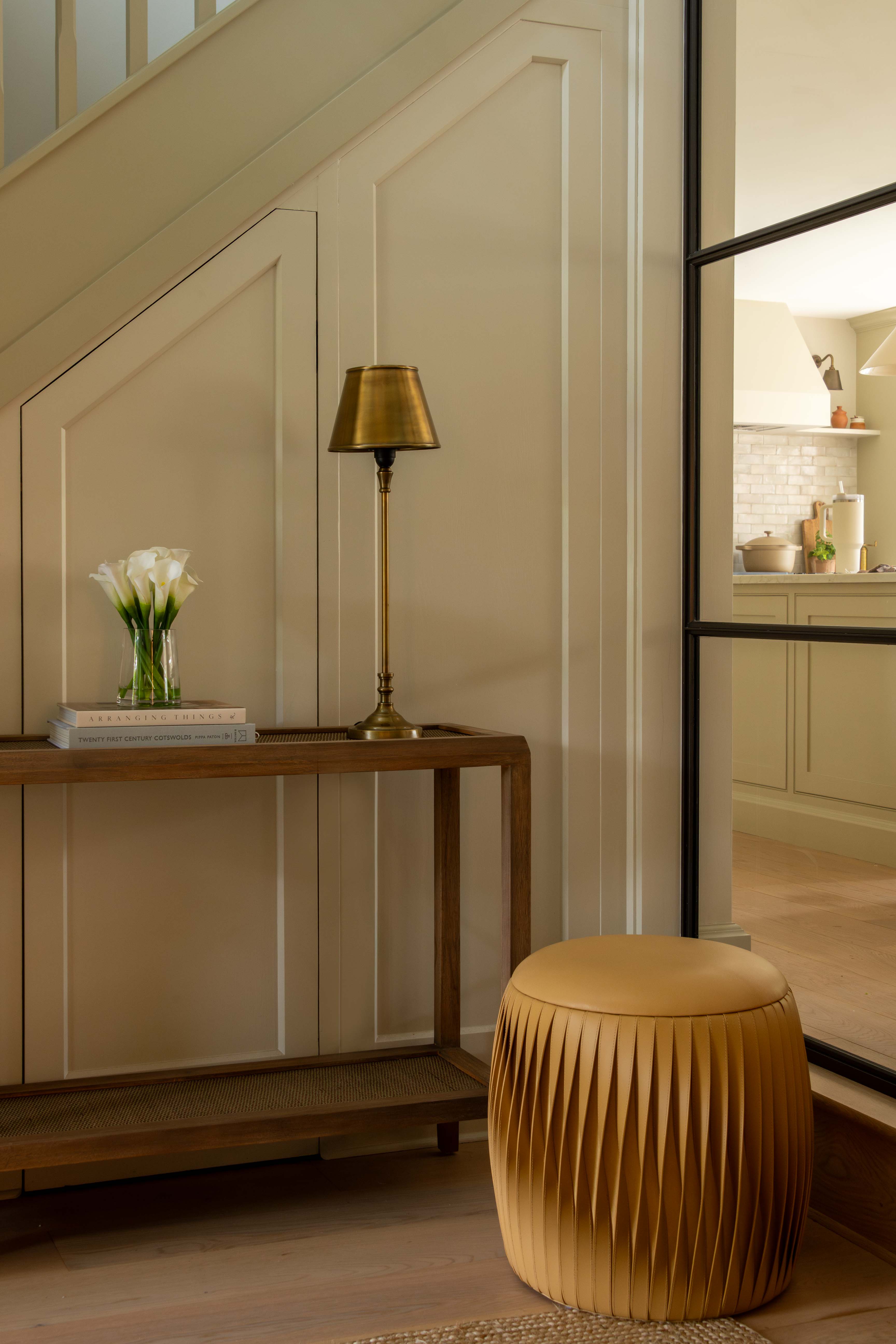 Modern interior with a wooden console table, gold lamp, and beige stool.