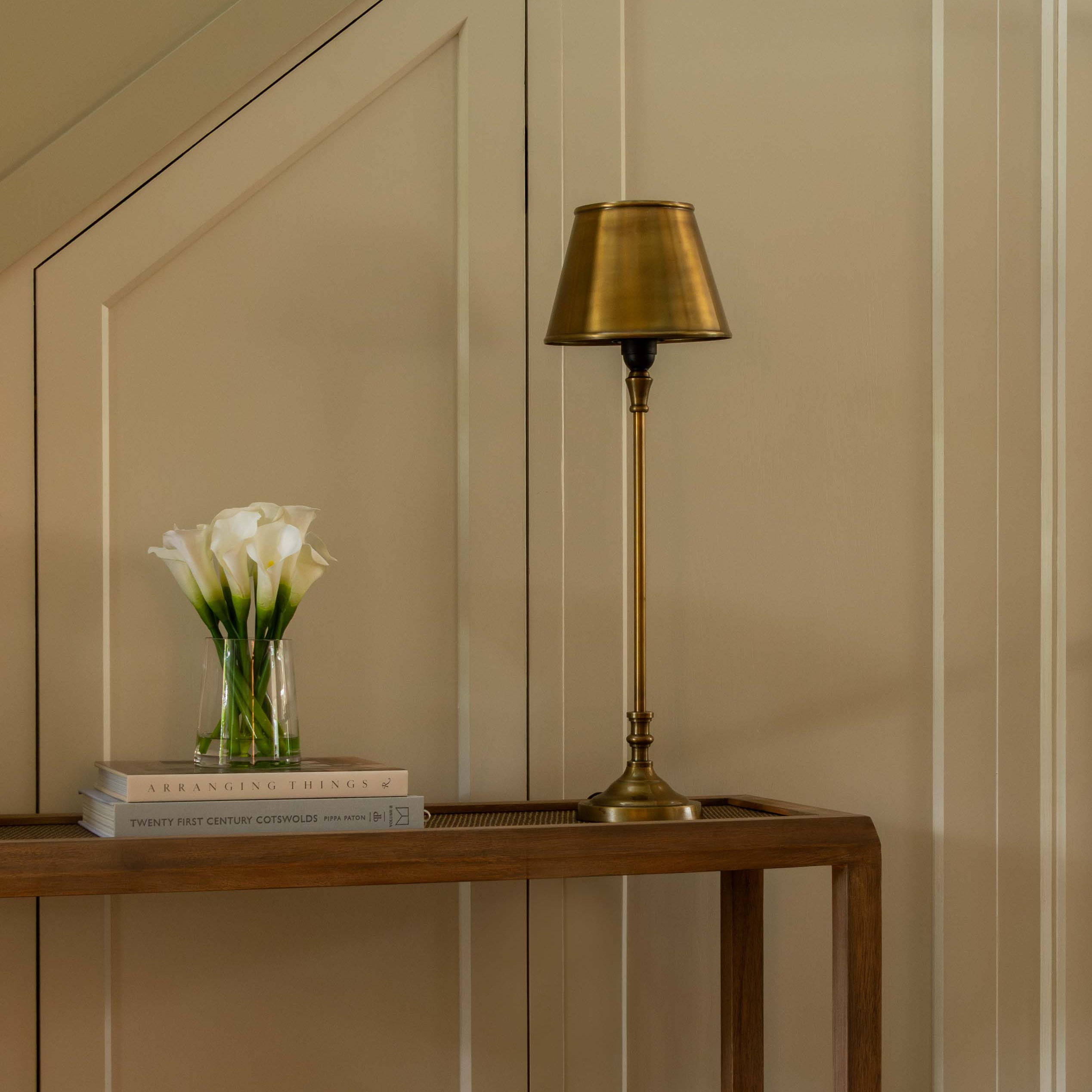 Modern interior with a wooden console table, gold lamp, and beige stool.