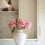 Bring effortless charm to your space with this beautifully crafted faux pink hydrangea, sold individually for versatile styling. Featuring lush, lifelike petals in soft blush tones and realistic green leaves, this artificial stem adds a delicate, romantic touch to any interior arrangement. Whether styled in a vase on your kitchen island, as shown, or combined with other stems for a fuller bouquet, it offers lasting beauty without maintenance.

Perfect for home décor, weddings, or gifting, this faux pink hyd