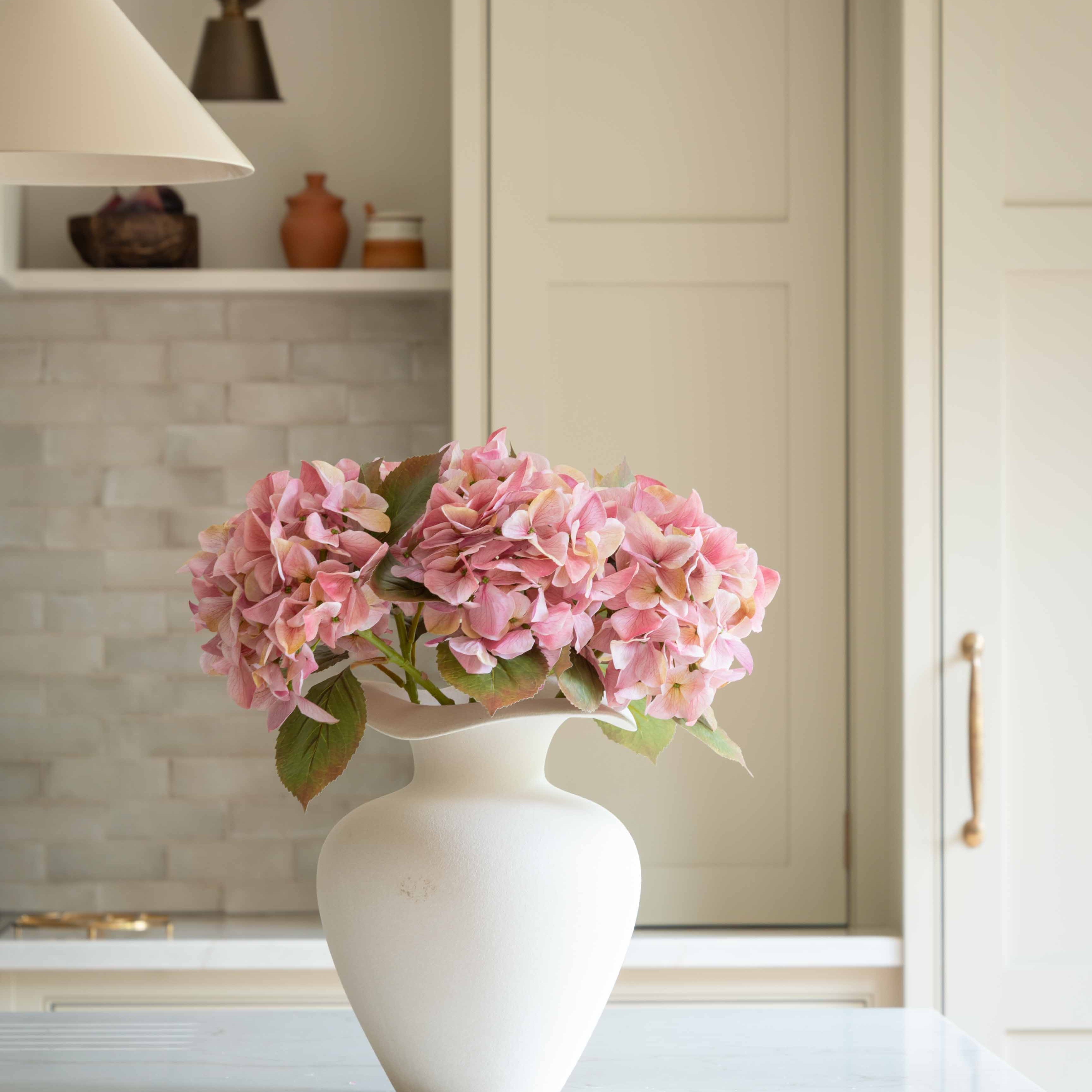 Bring effortless charm to your space with this beautifully crafted faux pink hydrangea, sold individually for versatile styling. Featuring lush, lifelike petals in soft blush tones and realistic green leaves, this artificial stem adds a delicate, romantic touch to any interior arrangement. Whether styled in a vase on your kitchen island, as shown, or combined with other stems for a fuller bouquet, it offers lasting beauty without maintenance.

Perfect for home décor, weddings, or gifting, this faux pink hyd