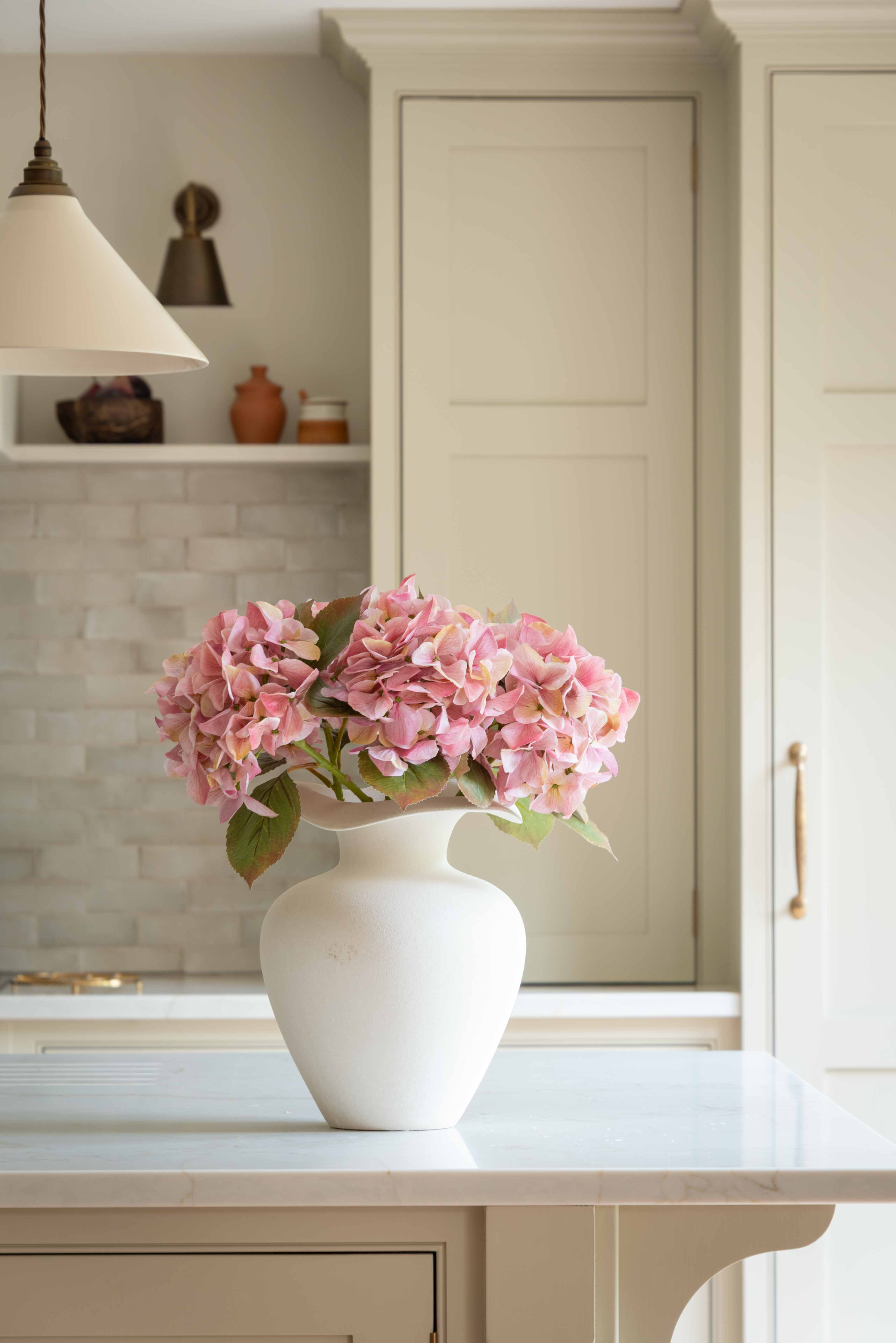 Bring effortless charm to your space with this beautifully crafted faux pink hydrangea, sold individually for versatile styling. Featuring lush, lifelike petals in soft blush tones and realistic green leaves, this artificial stem adds a delicate, romantic touch to any interior arrangement. Whether styled in a vase on your kitchen island, as shown, or combined with other stems for a fuller bouquet, it offers lasting beauty without maintenance.

Perfect for home décor, weddings, or gifting, this faux pink hyd