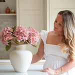 Bring effortless charm to your space with this beautifully crafted faux pink hydrangea, sold individually for versatile styling. Featuring lush, lifelike petals in soft blush tones and realistic green leaves, this artificial stem adds a delicate, romantic touch to any interior arrangement. Whether styled in a vase on your kitchen island, as shown, or combined with other stems for a fuller bouquet, it offers lasting beauty without maintenance.

Perfect for home décor, weddings, or gifting, this faux pink hyd