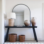 Arch-shaped mirror with black trim sitting on a console table.
