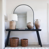 Arch-shaped mirror with black trim sitting on a console table.