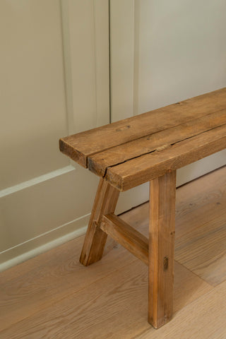 Wooden bench against a beige wall on a wooden floor