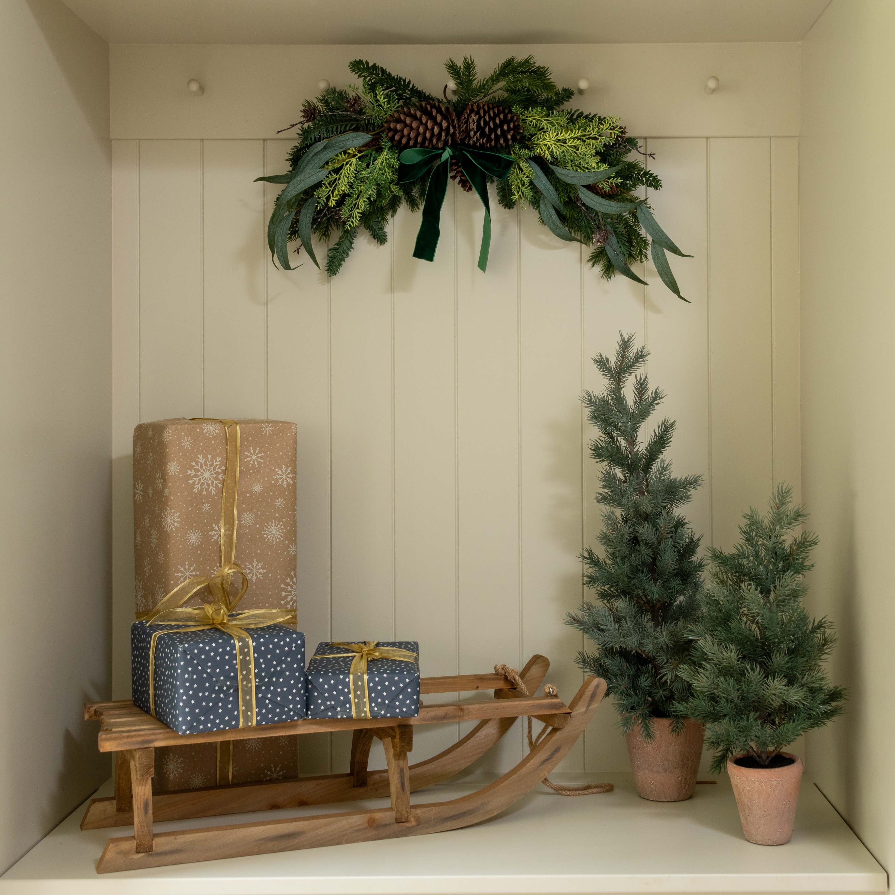 Decorative setup with Christmas trees, presents, and a sled in a white cabinet.