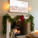 Living room with a fireplace decorated for Christmas, featuring greenery and a red bow.