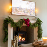 Living room with a fireplace decorated for Christmas, featuring greenery and a red bow.