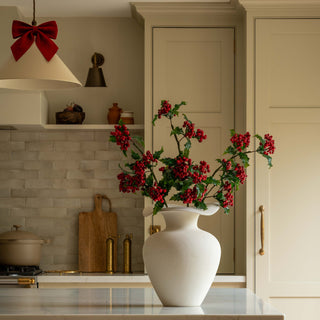 Faux holly and ivy stems with red berries in a vase on a kitchen worktop at Christmas