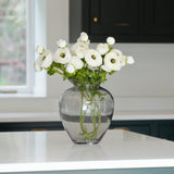 Glass vase filled with lifelike artificial white ranunculus stems on a kitchen countertop