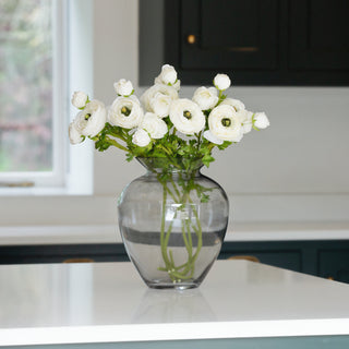 Glass vase filled with lifelike artificial white ranunculus stems on a kitchen countertop